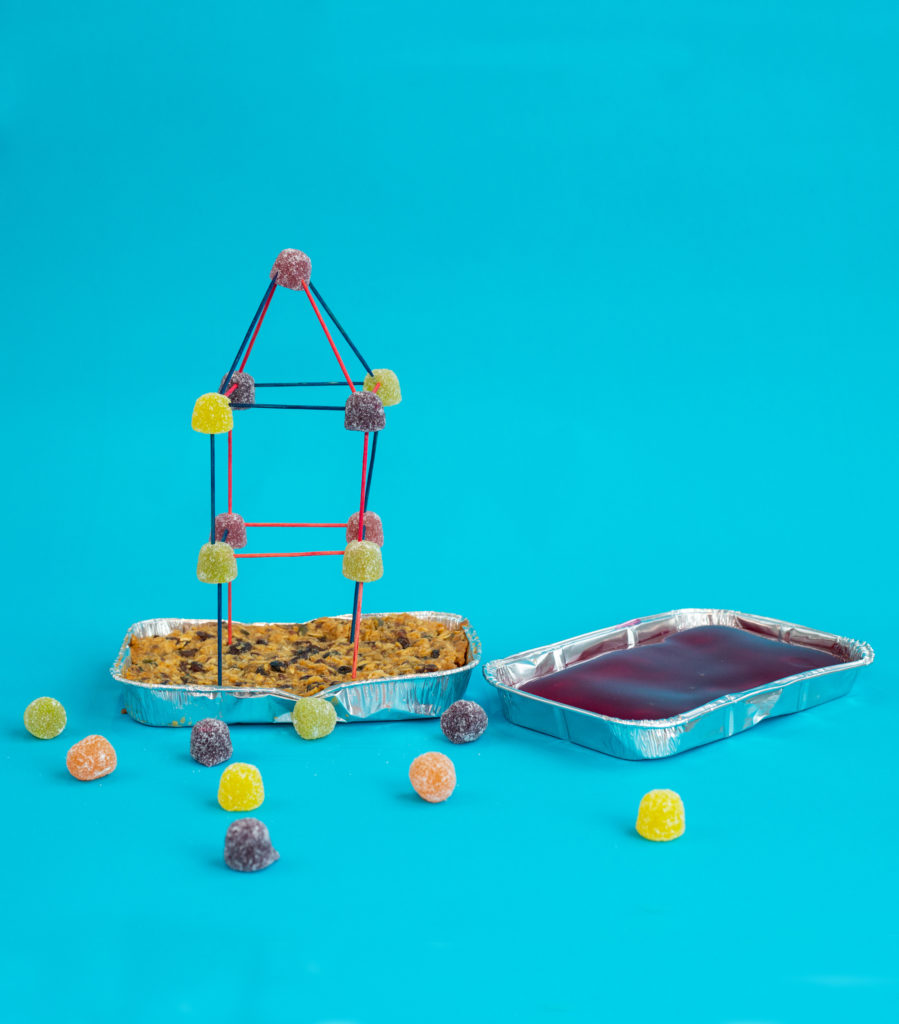 Two foil trays one filled with jelly/jello and one flapjack. The flapjack tray has a tower made from toothpicks and gummy sweets in the flapjack base. For an earthquake science experiment .