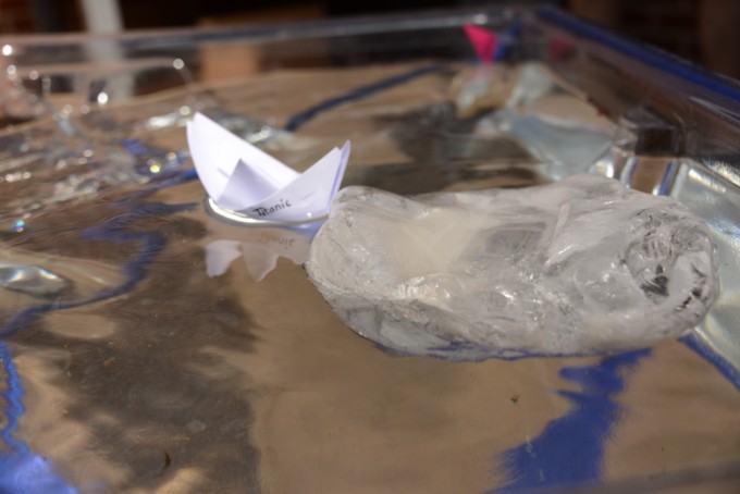 a lump of ice and a paper boat floating in a water table for a science experiment about the Titanic