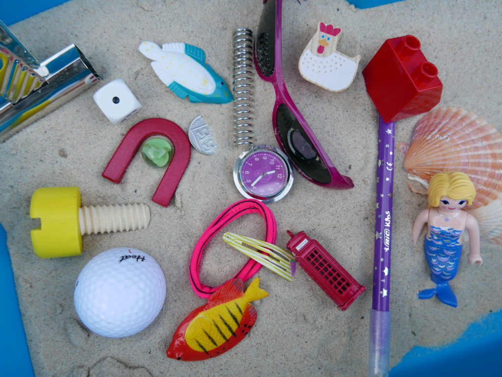 Ariel's Treasures set up as a sorting activity for kids. Image shows magnets, hair bands, plastic fish etc in sand ready to be sorted