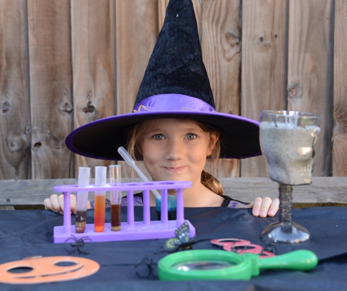 Little girl with a witches hat on sat behind a table of spooky potions