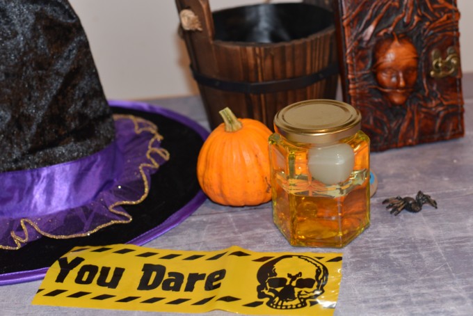 Witchy Density Jar made with oil ad water sat in a background of a witches hat and Halloween props