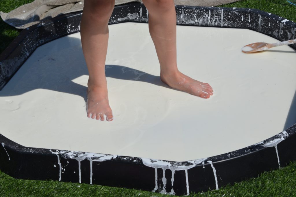 child standing in a giant black tray of oobleck
