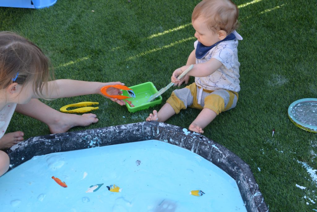 toddler sat next to a huge tray of blue oobleck