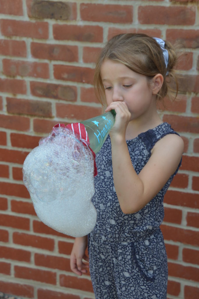 Child blowing down a a bottle to make a snake of bubbles