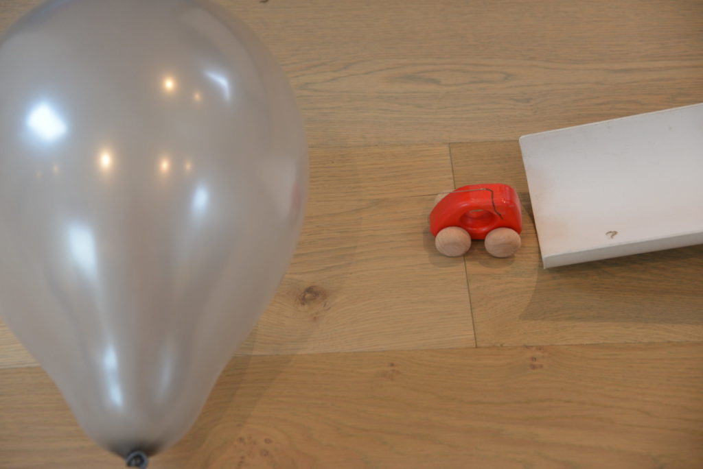 a wooden toy car with a needle attached heading towards a balloon as part of a Rube Goldberg machine