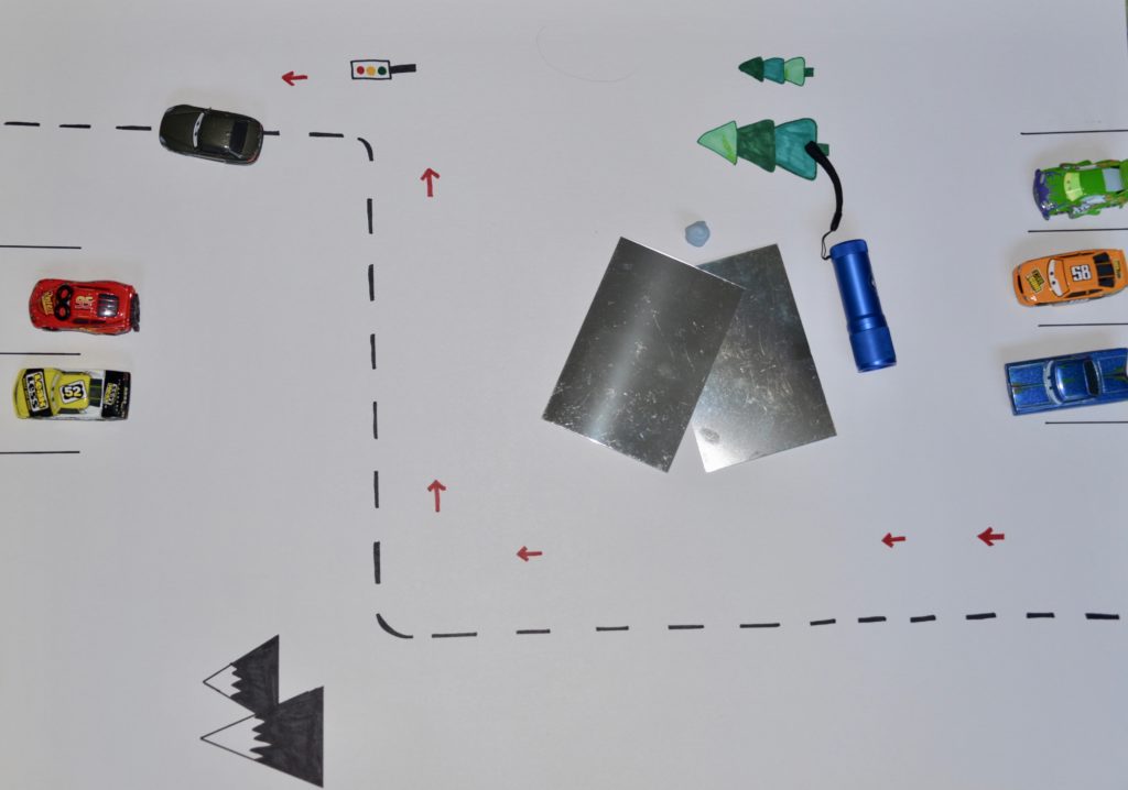 light maze idea. Image shows a large sheet of card with toy cars, mirrors and a torch.