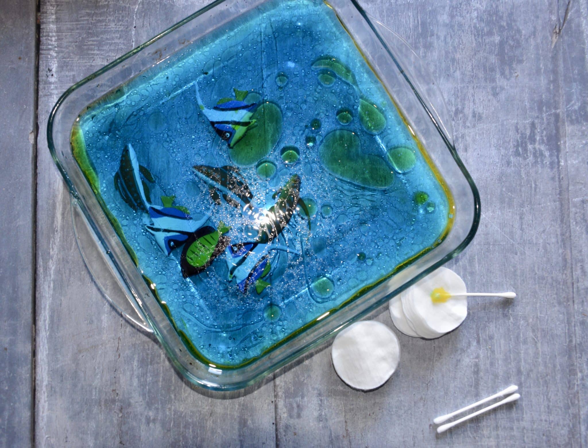 oil spill activity. Image shows a glass tray filled with blue water and a layer of vegetable oil floating on the top.