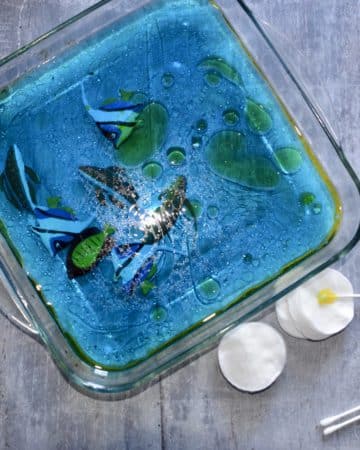 oil spill activity. Image shows a glass tray filled with blue water and a layer of vegetable oil floating on the top.