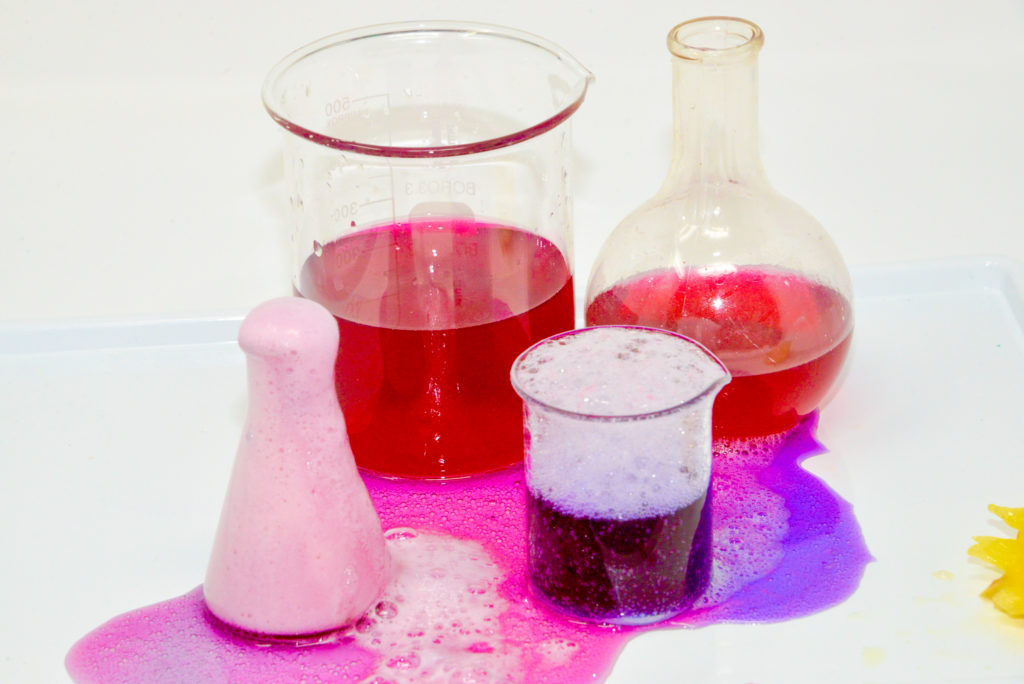 Beakers containing several pink and red fizzy potions for a Valentine's day science activity