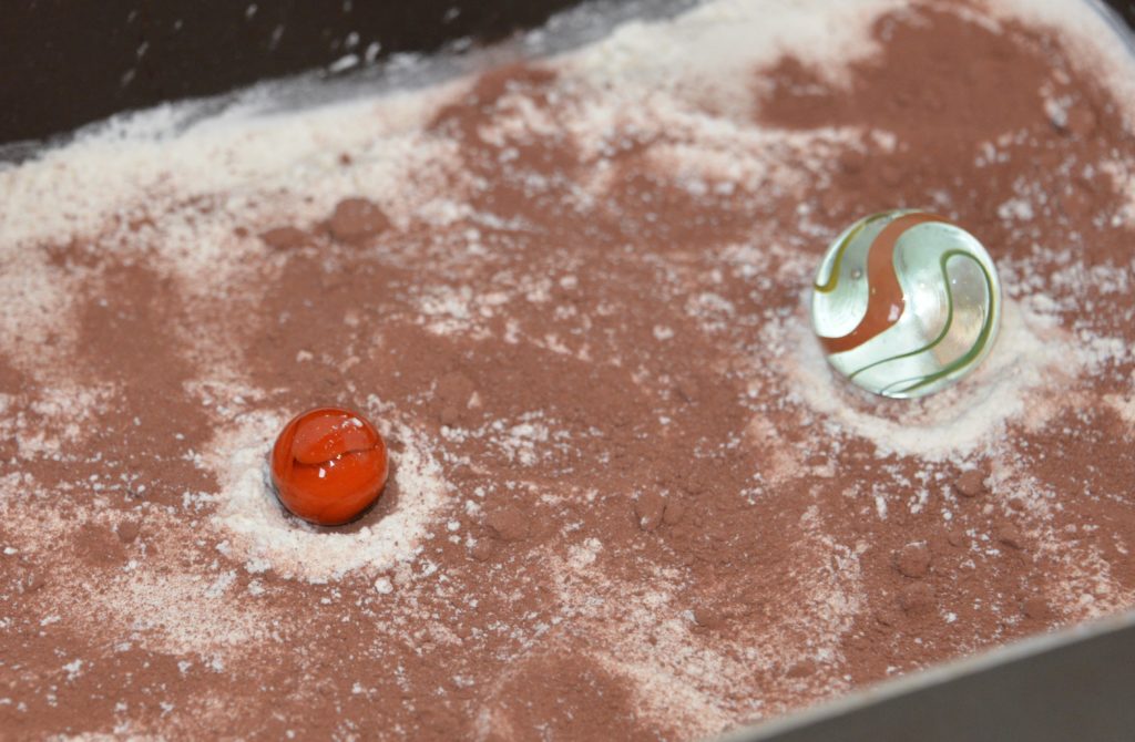 marbles that have been dropped in a tray filled with flour and hot chocolate powder to demonstrate craters falling to Earth