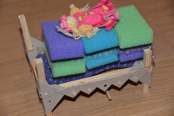 Wooden bed frame covered with sponges, bubble wrap and felt with a small doll sat on top