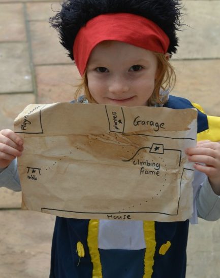 child dressed as a pirate holding a coffee and tea stained treasure map