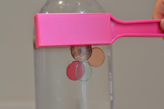 magnet sensory bottle. Plastic bottle filled with water. Several magnetic discs and coins are inside. A pink magnet wand is on the outside.