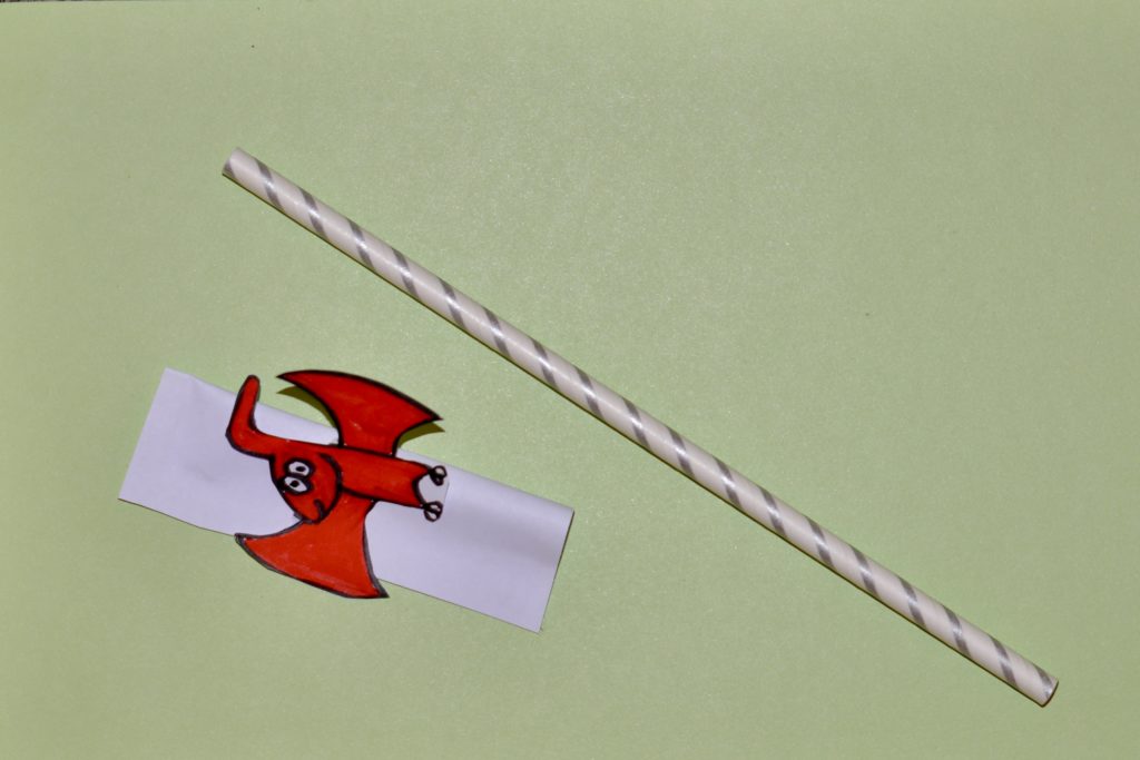 Materiales para el experimento del cohete de paja: una pajita y un pequeño trozo de papel doblado con un pterodáctilo rojo al final