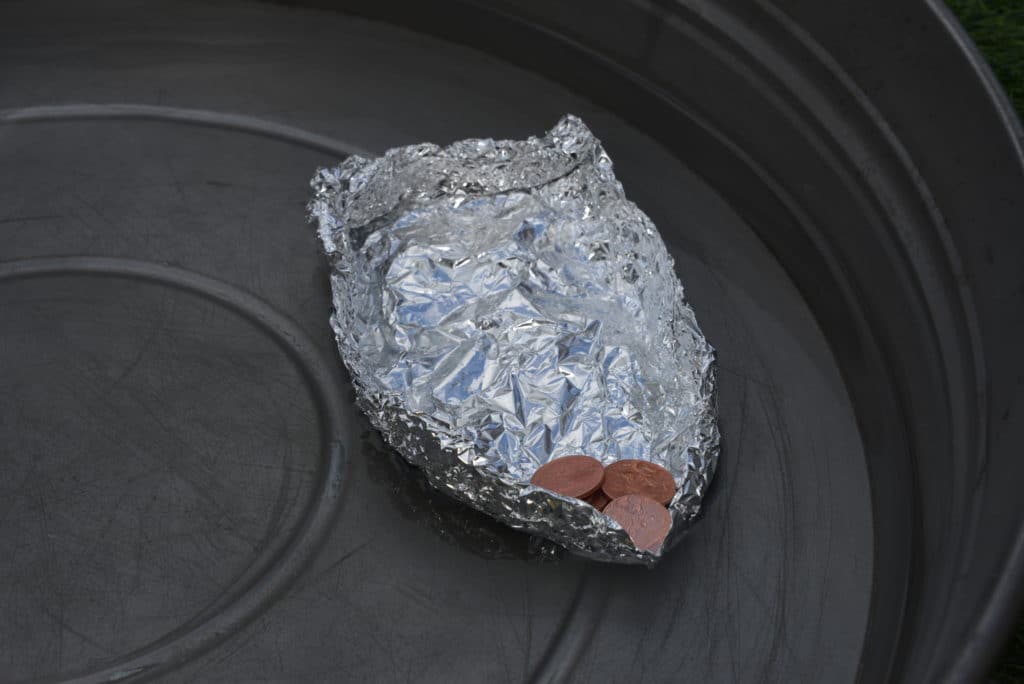 foil boat with a coin inside floating in a large flat tin of water