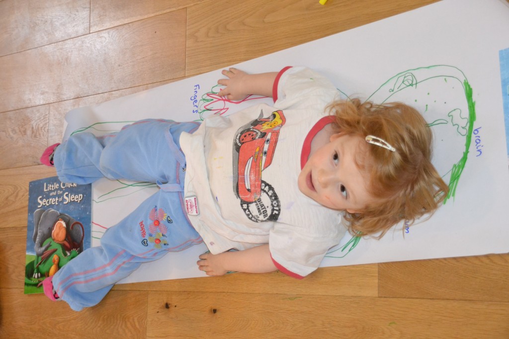 Image of a child lying on a large sheet of paper ready to be drawn around for an activity about the human body