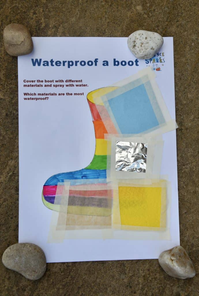 sheet of A4 paper on the ground with a drawing of a wellington boot. The boot has been coloured with felt tip and different materials have been taped over the top for a waterproofing science experiment.