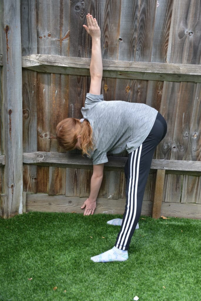 Girl measuring her arm span against a  fence