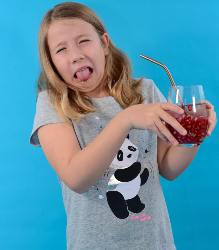 Image of a girl pulling an ick face holding a red blood cell cocktail containing soda water, pomegranate and pineapple