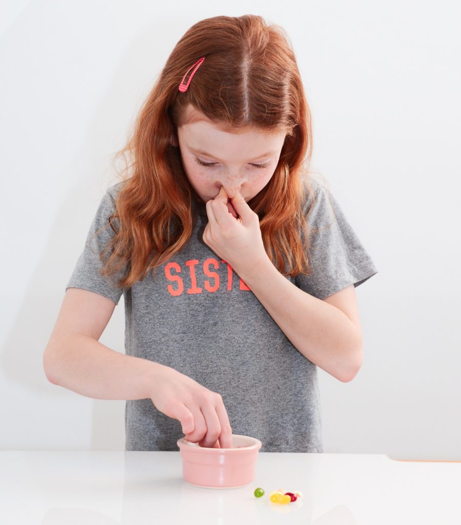 How is smell linked to taste? Image of a girl holding her nose and eating jelly beans