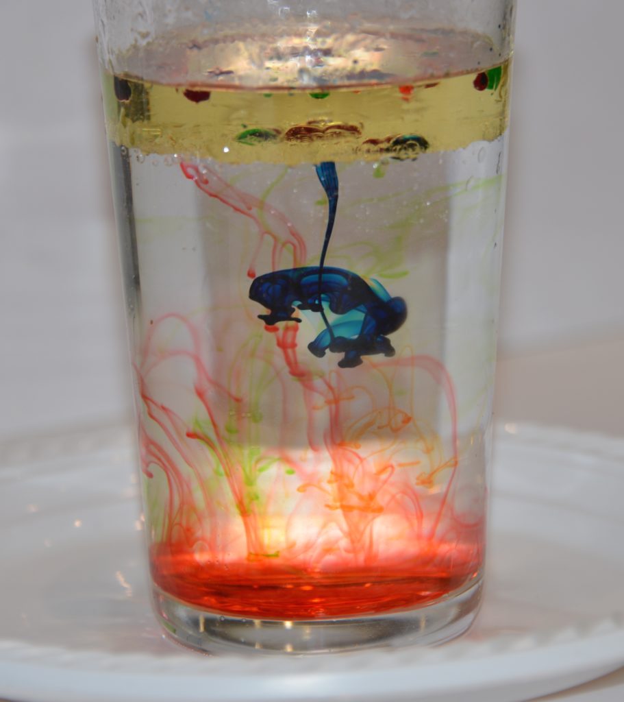 firework in a jar. Image shows a glass filled with water with a layer of oil on the top. Food colouring bursts through the oil into the water to give a firework effect.