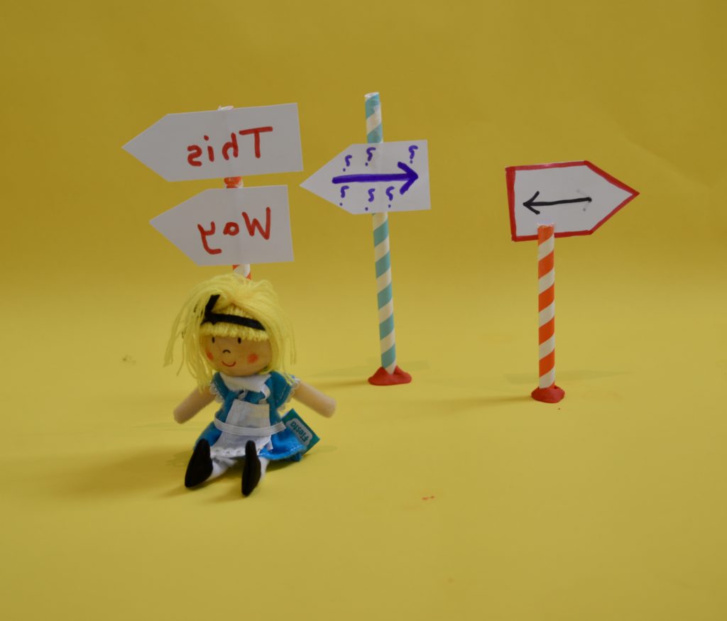 Image of an Alice in Wonderland puppet with arrows on signs behind her for a light refraction science investigation