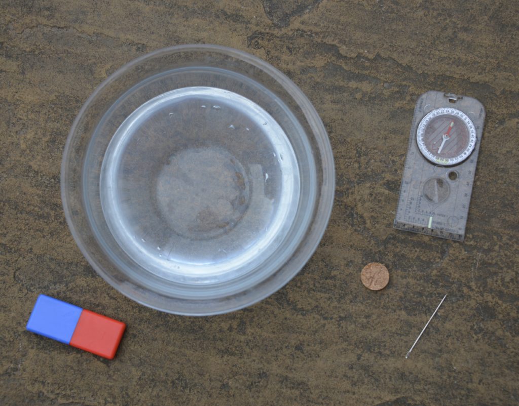 Bowl of water, compass, needle, slice of cork and a magnet ready to make a compass using a magnet