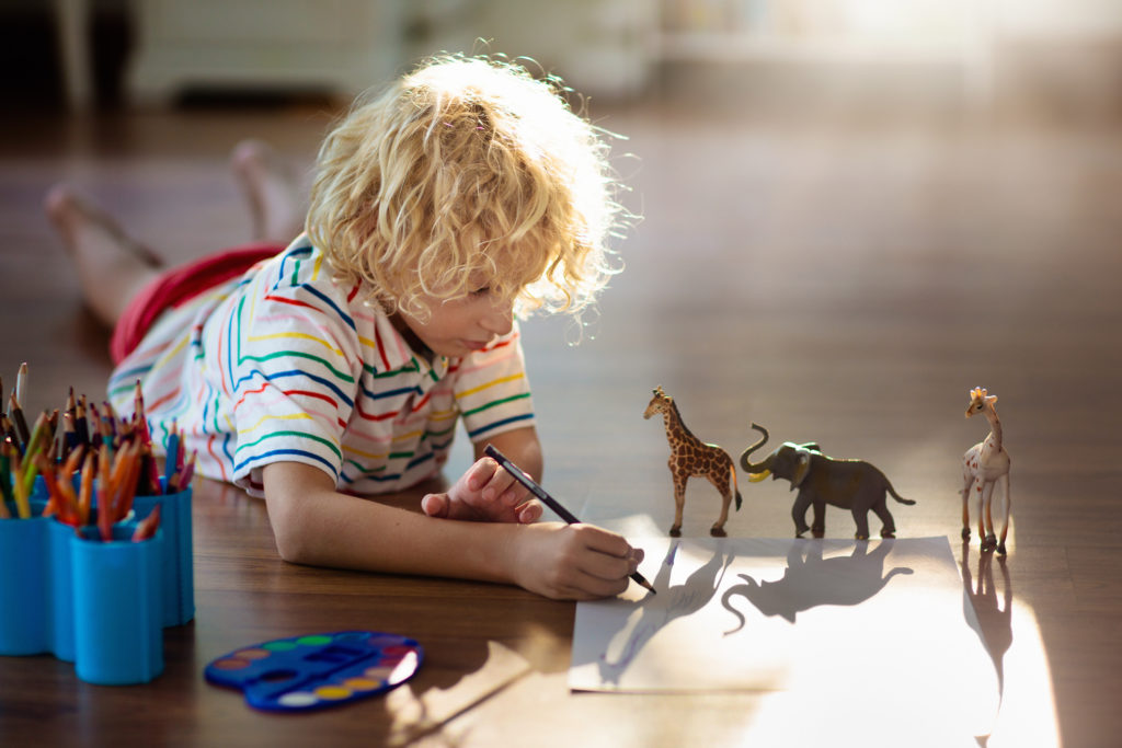 child drawing around plastic toy animals