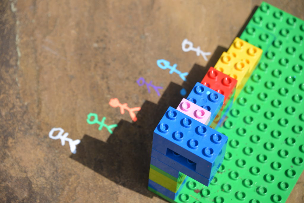 Image of a shadow made with duplo and drawings on the ground to make a picture using the shadow. Image shows a shadow of steps with stick people drawn on the floor stood on each step.