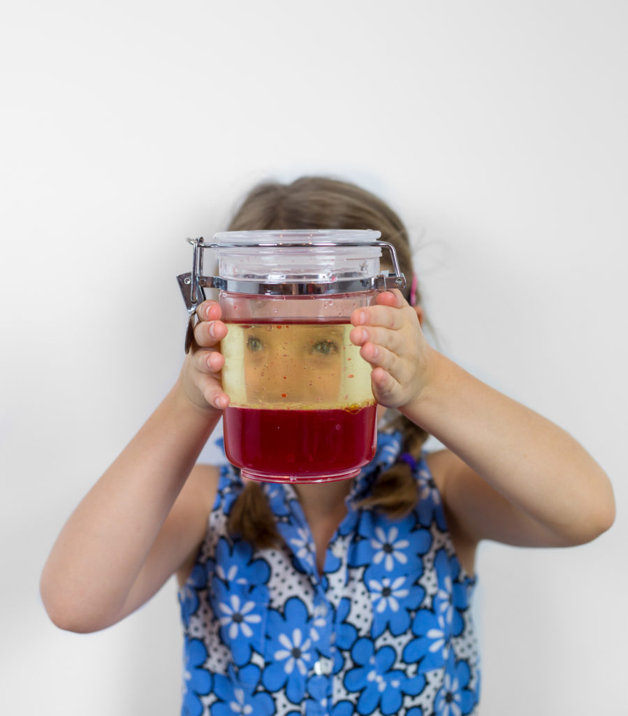 girl looking through a jar of water and oil where the oil and water have separated