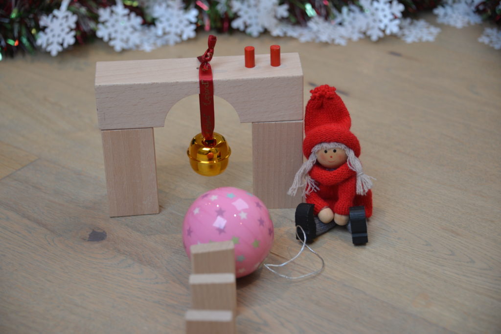dominoes crash into a bauble which hits a bell as part of a chain reaction with a Christmas theme