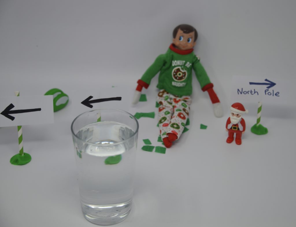 Image of an elf with a glass with an arrow drawn on paper behind it for a refraction experiment