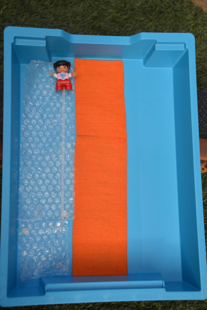 A large storage tray used to make a slide for a small toy. The tray is split into three lanes for a friction investigation. One lane is covered in felt, one bubble wrap and one left plain as the tray.