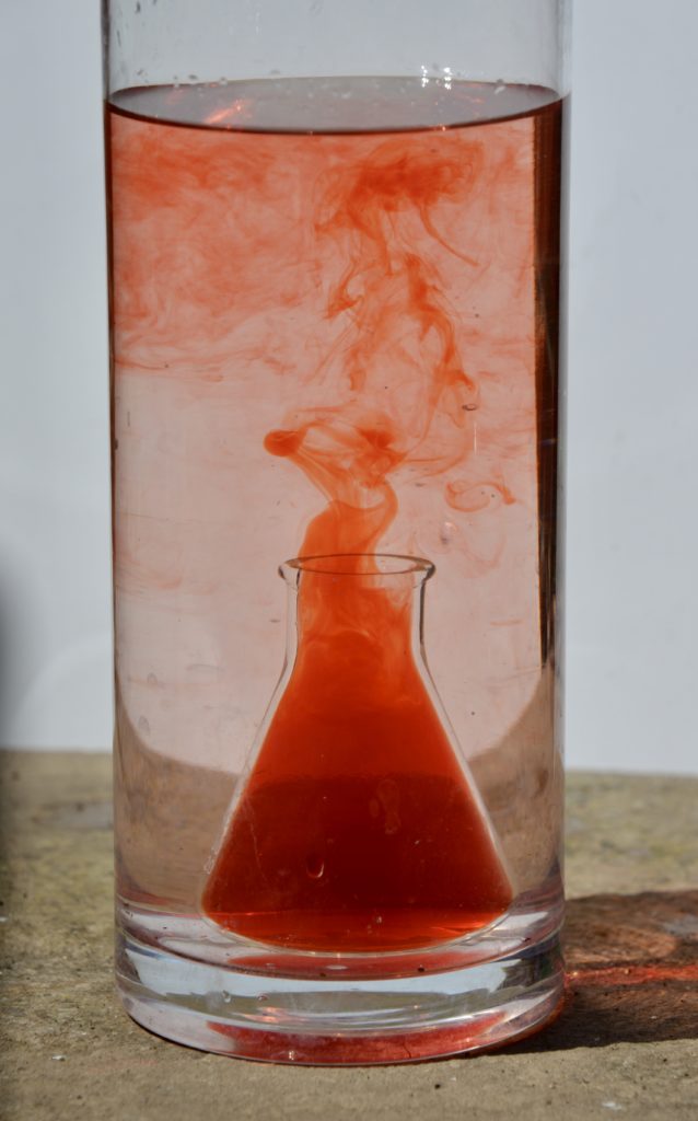 warm red water rises in a vase of clear cooler water