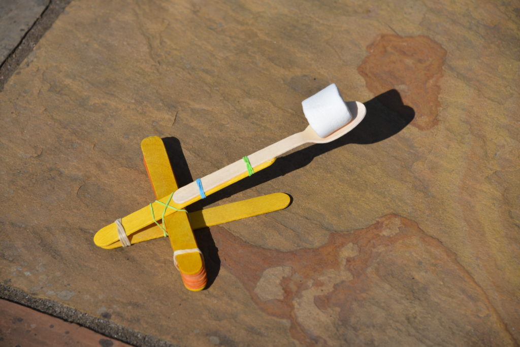 slingshot made from craft sticks with a wooden spoon as a launch arm and a marshmallow loaded ready to launch
