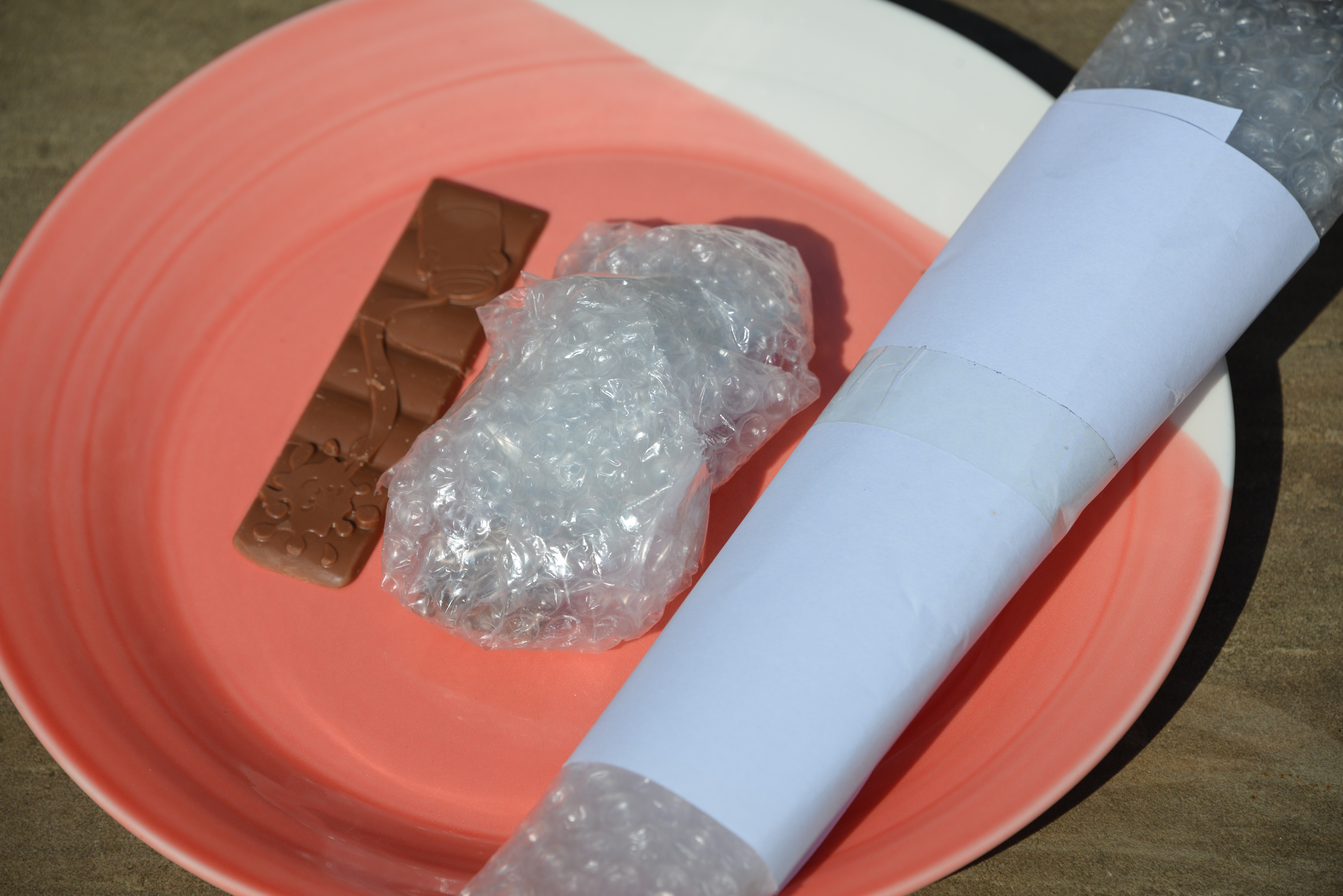 one small bar of chocolate uncovered, one covered in bubble wrap and one covered in bubble wrap and white paper