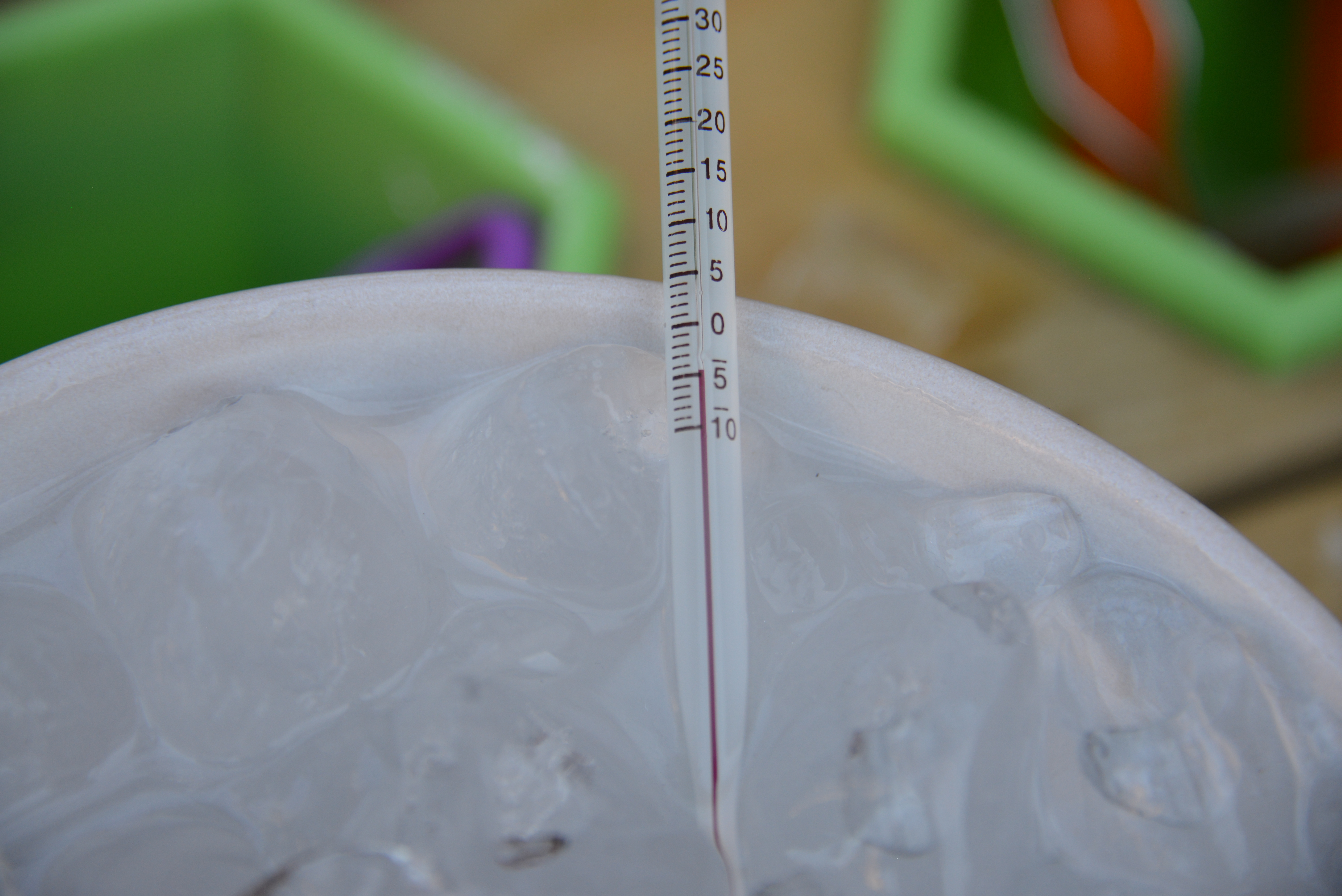 thermometer in a bowl of ice and water to show how adding salt reduces the temperature of the water to cool a drink