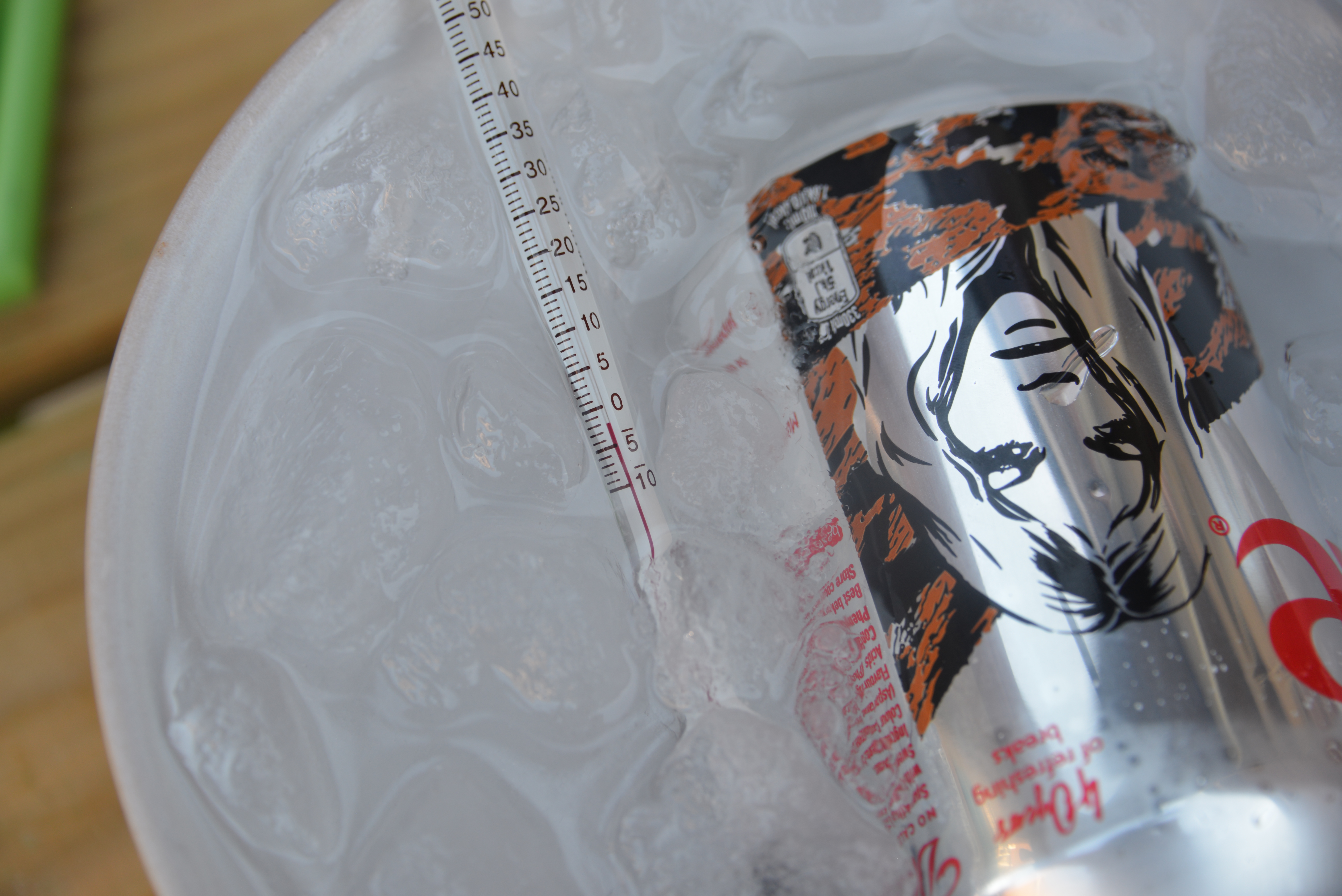 a thermometer in a bowl of ice and water with a can of drink for a science investigation