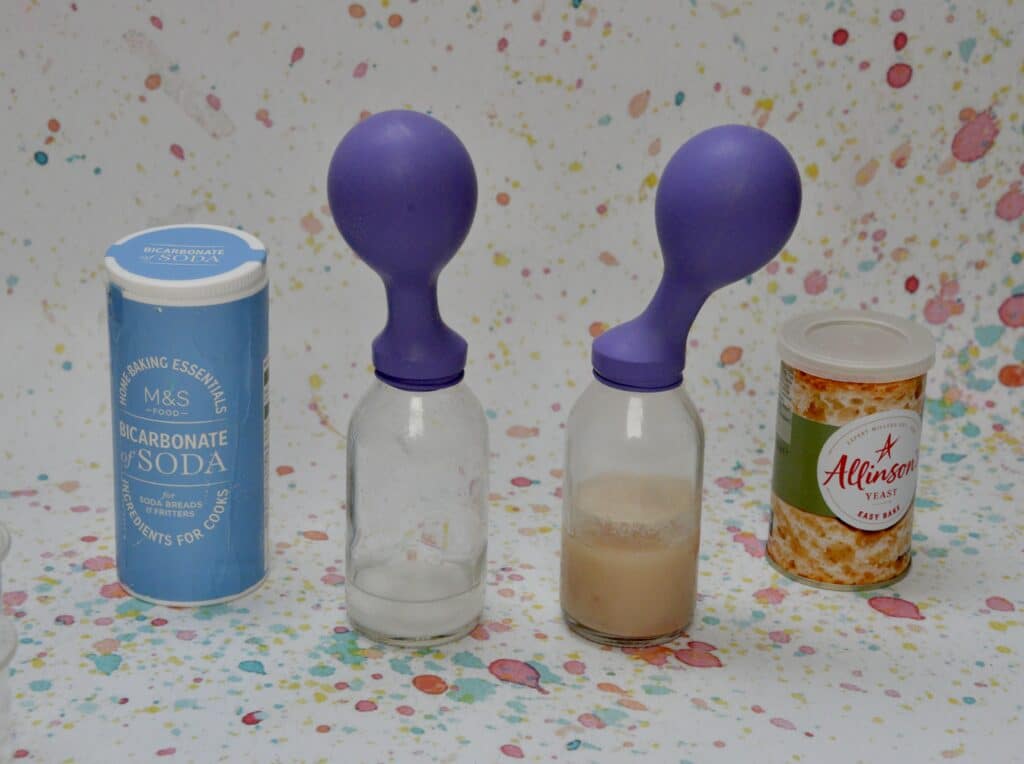 tub of bicarbonate of soda and dried yeast next to a small glass bottle with a balloon on top. The balloon are slightly inflated