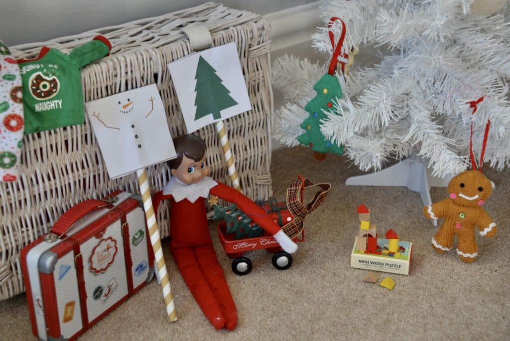 elf sat next to two straws one has the image of a Christmas tree on top and the other Christmas tree decorations