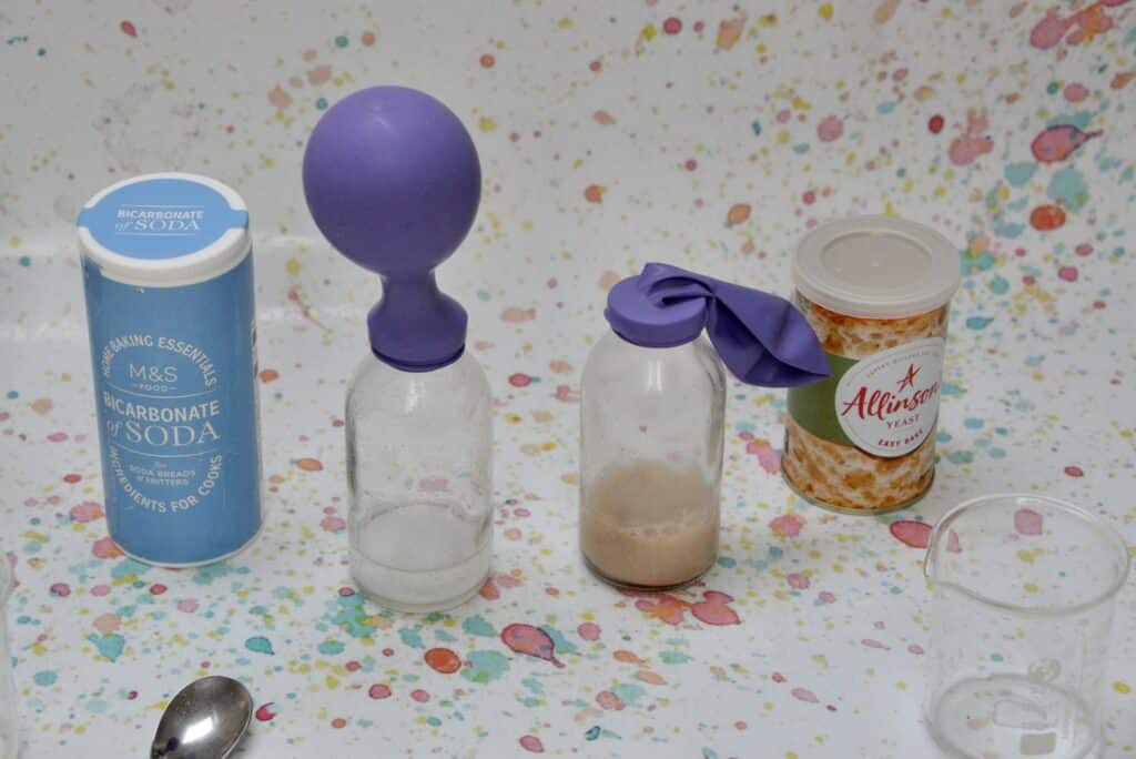 tub of bicarbonate of soda and dried yeast next to a small glass bottle with a balloon on top. The balloon are slightly inflated