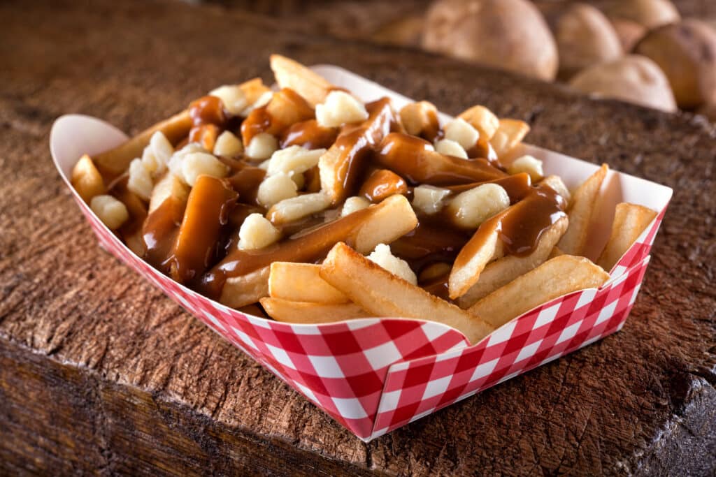 A serving of delicious poutine with french fries, cheese curds and gravy on a rustic wooden board.