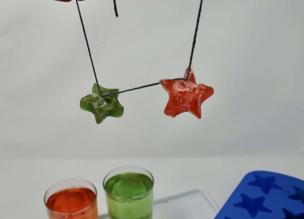 two coloured star ice cubes hanging from a string. Lift an ice cube with string experiment