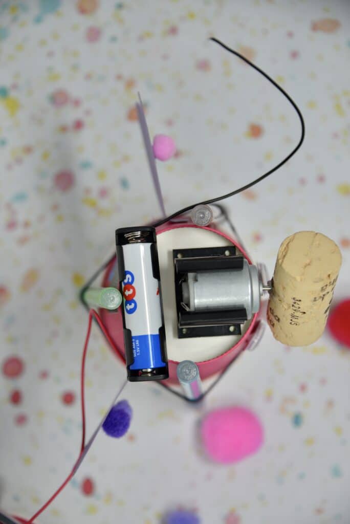 top down photo of a drawing robot showing an AA battery and holder, 1.5V motor with a cork attached.