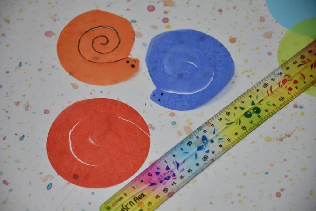 3 small snake shapes cut out from tissue paper and a colourful ruler