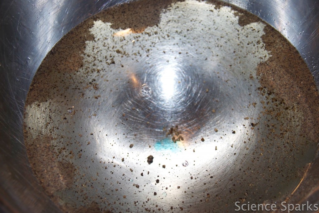a metal bowl filled with water, black pepper has been sprinkled over the surface and dish soap used to disrupt the surface tension moving the pepper to the edges