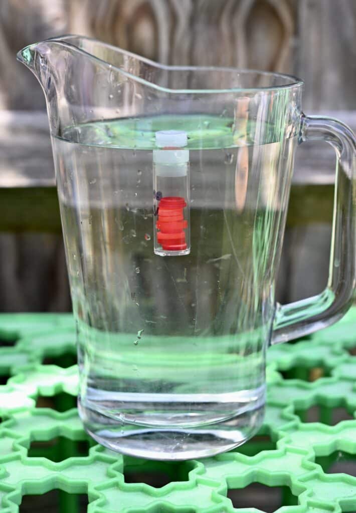 large jug of water with a test tube half full of water floating near the surface.