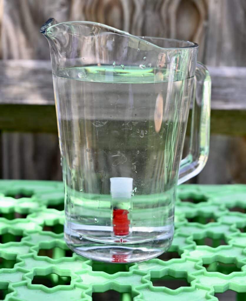 A large jug of water with a smell test tube inside. The test tube has a lid and it full of water.