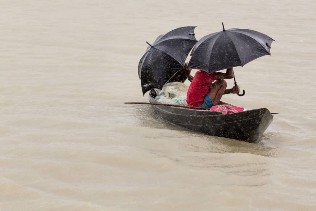 arisal, Bangladesh - July 12, 2016: Men in a wooden canoe sheltering under umbrellas from the monsoon rain. 
