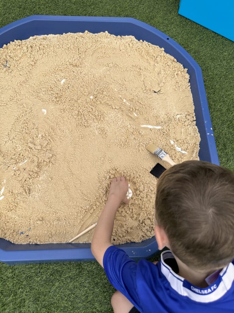 Child brushing sand of white air drying clay dinosaur bones for a paleontologist activity